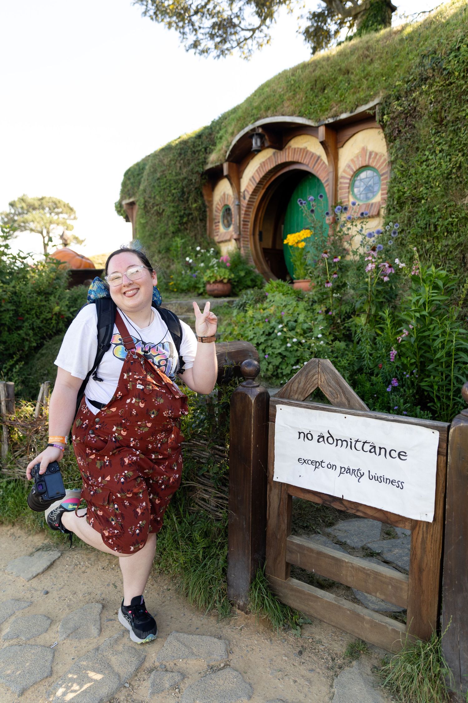 Tourist poses by a Hobbit hole entrance with round doors at Hobbiton Movie Set in New Zealand.