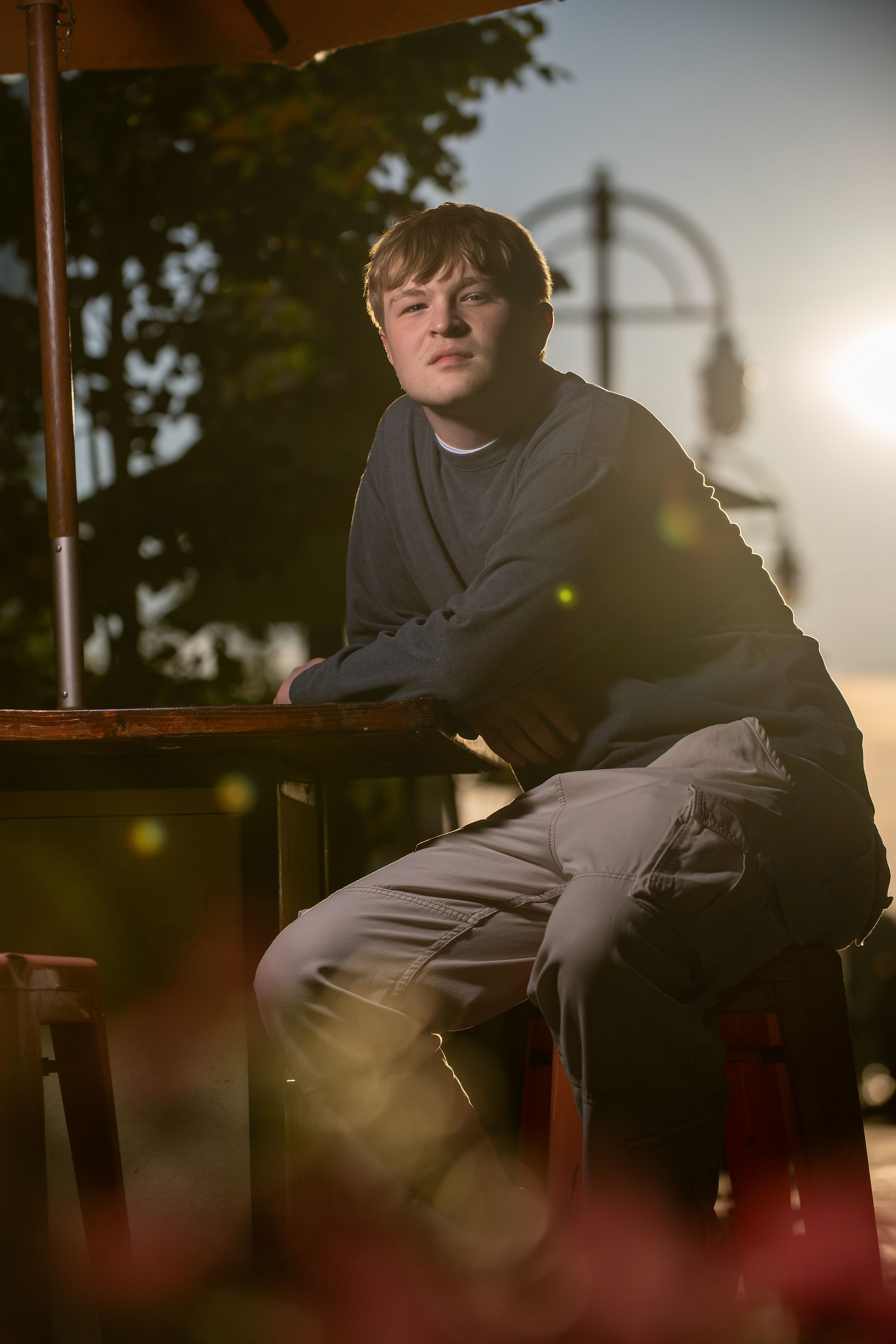 Young man in gray sweatshirt sitting outdoors at golden hour with warm sunlight and bokeh effect.