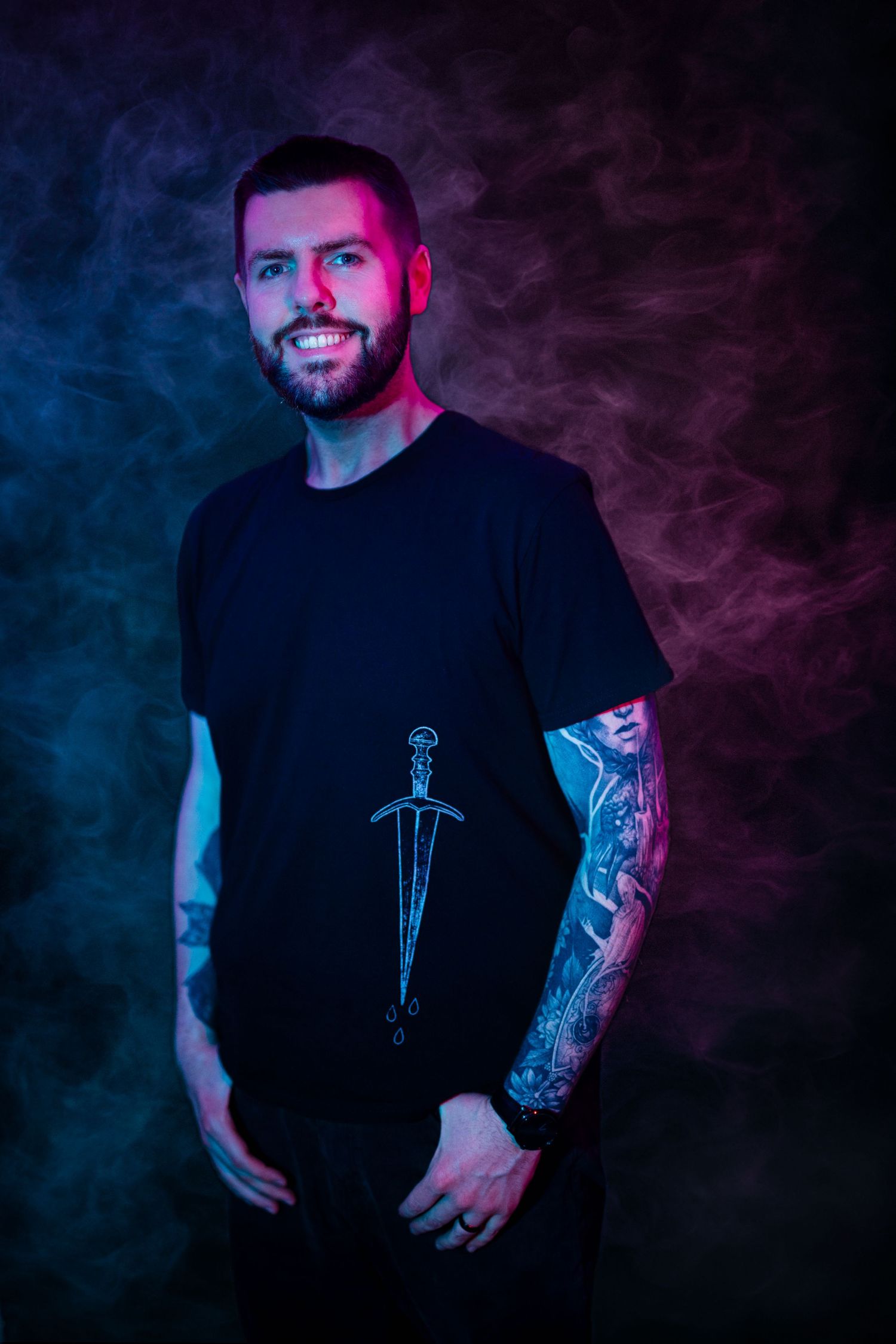 Portrait of man with tattoo in black shirt against colorful smoke backdrop.