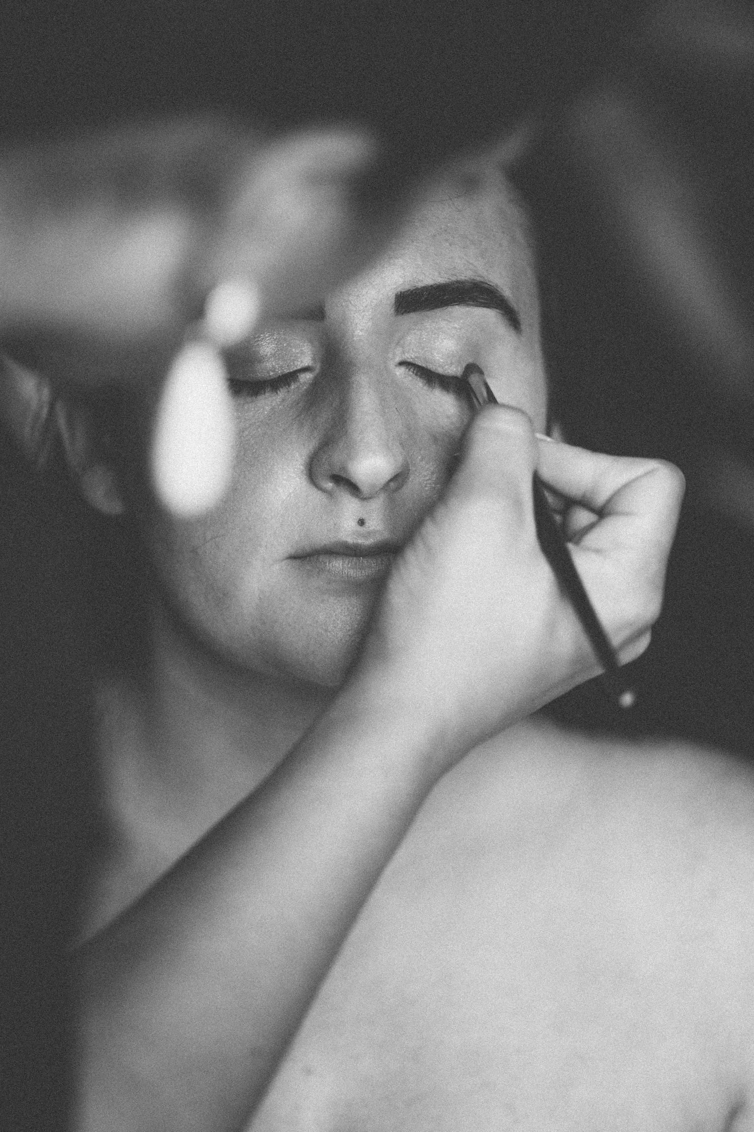 Black and white close-up shot showing makeup application with eyebrow brush.