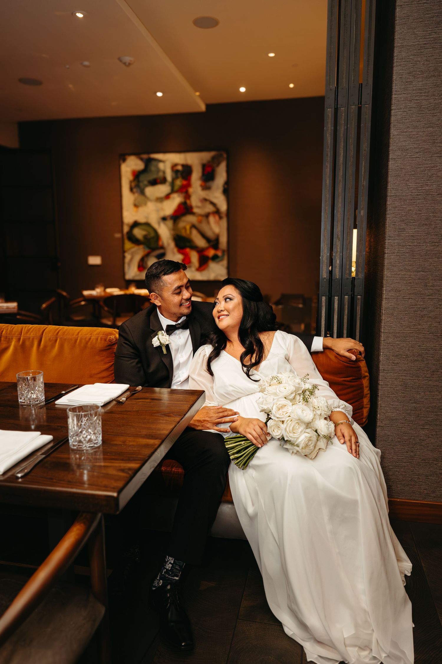 Newlyweds share a playful moment in an elegant indoor venue with mood lighting.