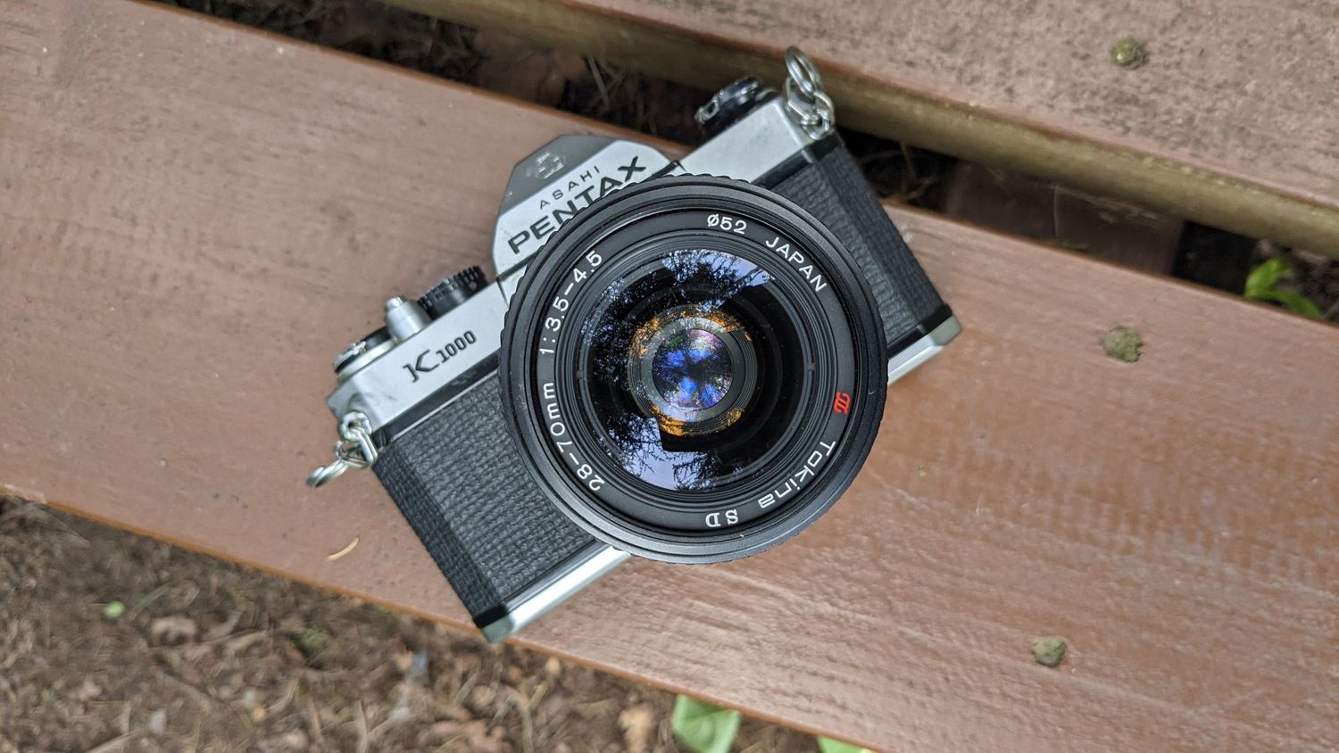 Vintage Pentax film camera with standard lens lying on wooden surface.