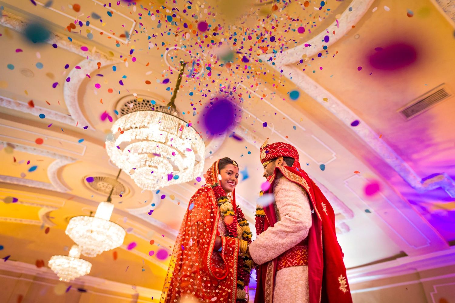 Colorful confetti falls from the ceiling as a couple celebrates during their traditional Indian wedding ceremony.