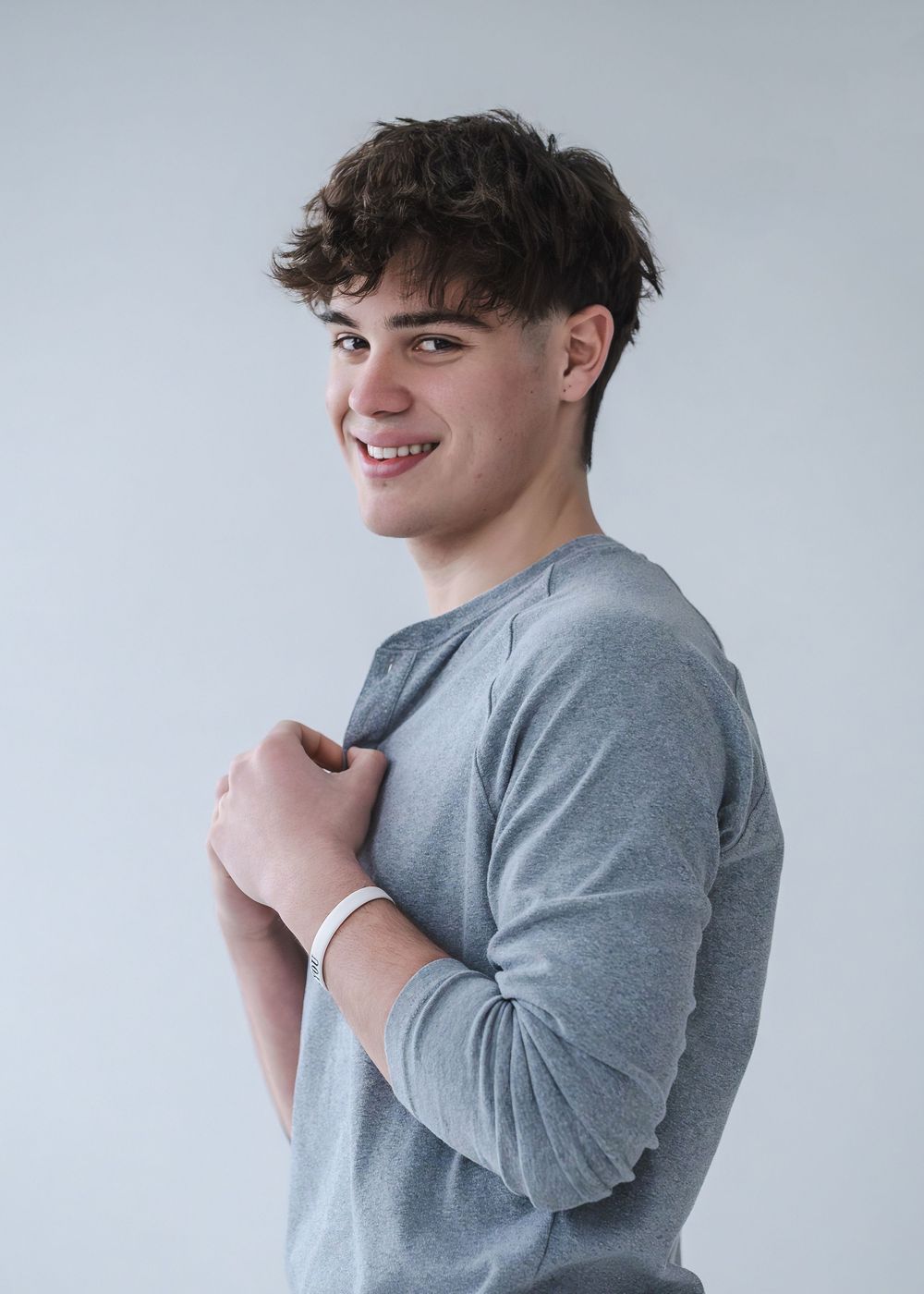 Smiling young man in gray long sleeve shirt posing against white background with hands crossed at chest.