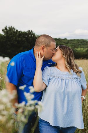 couple blue shirts in field of wildflowers and grass kissing