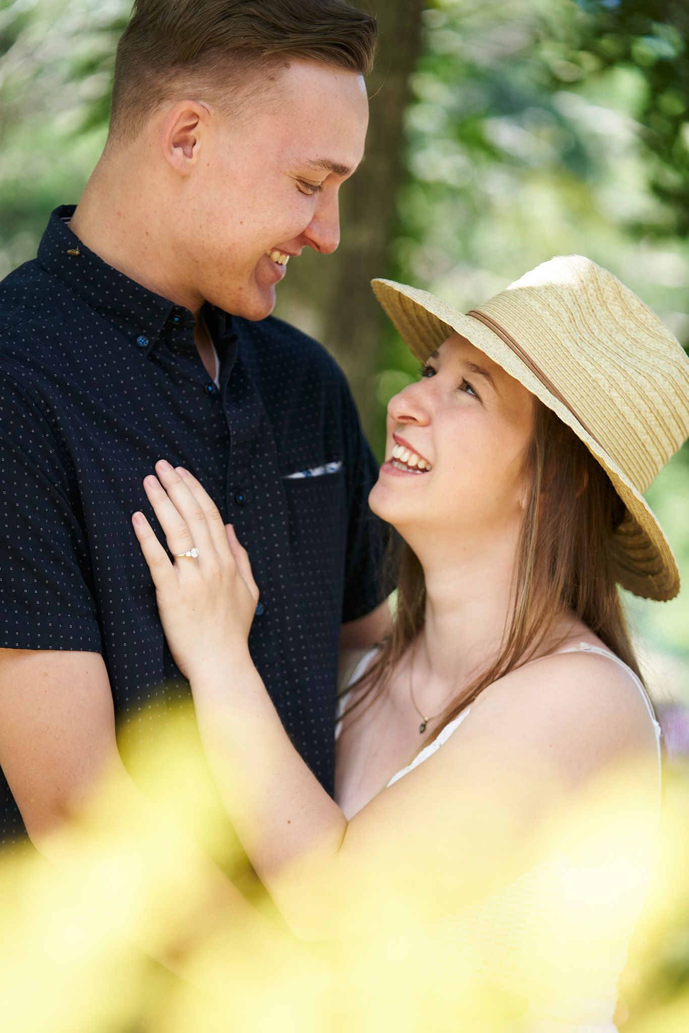 A couple shares a romantic moment outdoors, with her wearing a straw hat and him in a navy polo shirt.