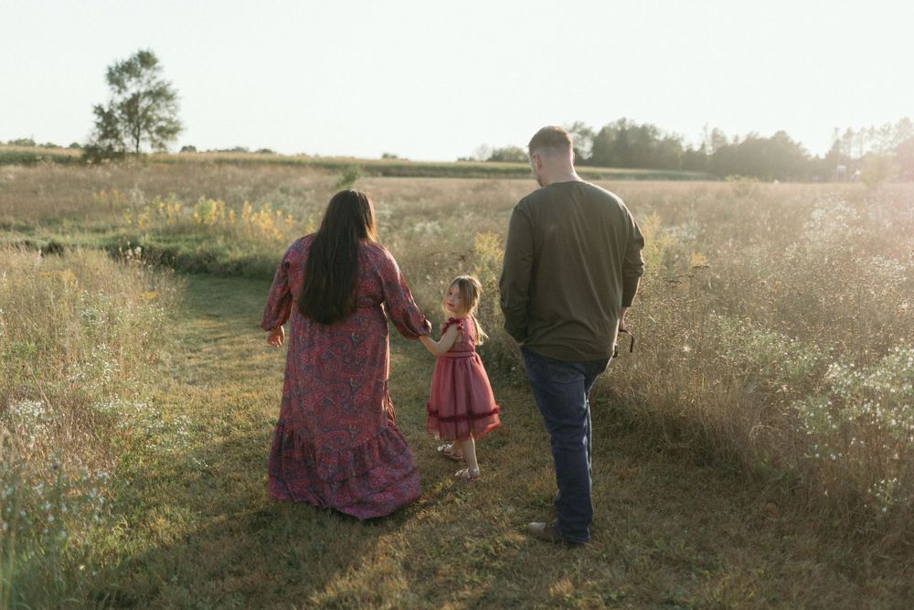 A family walks together on a sunlit path through a golden autumn field at sunset.