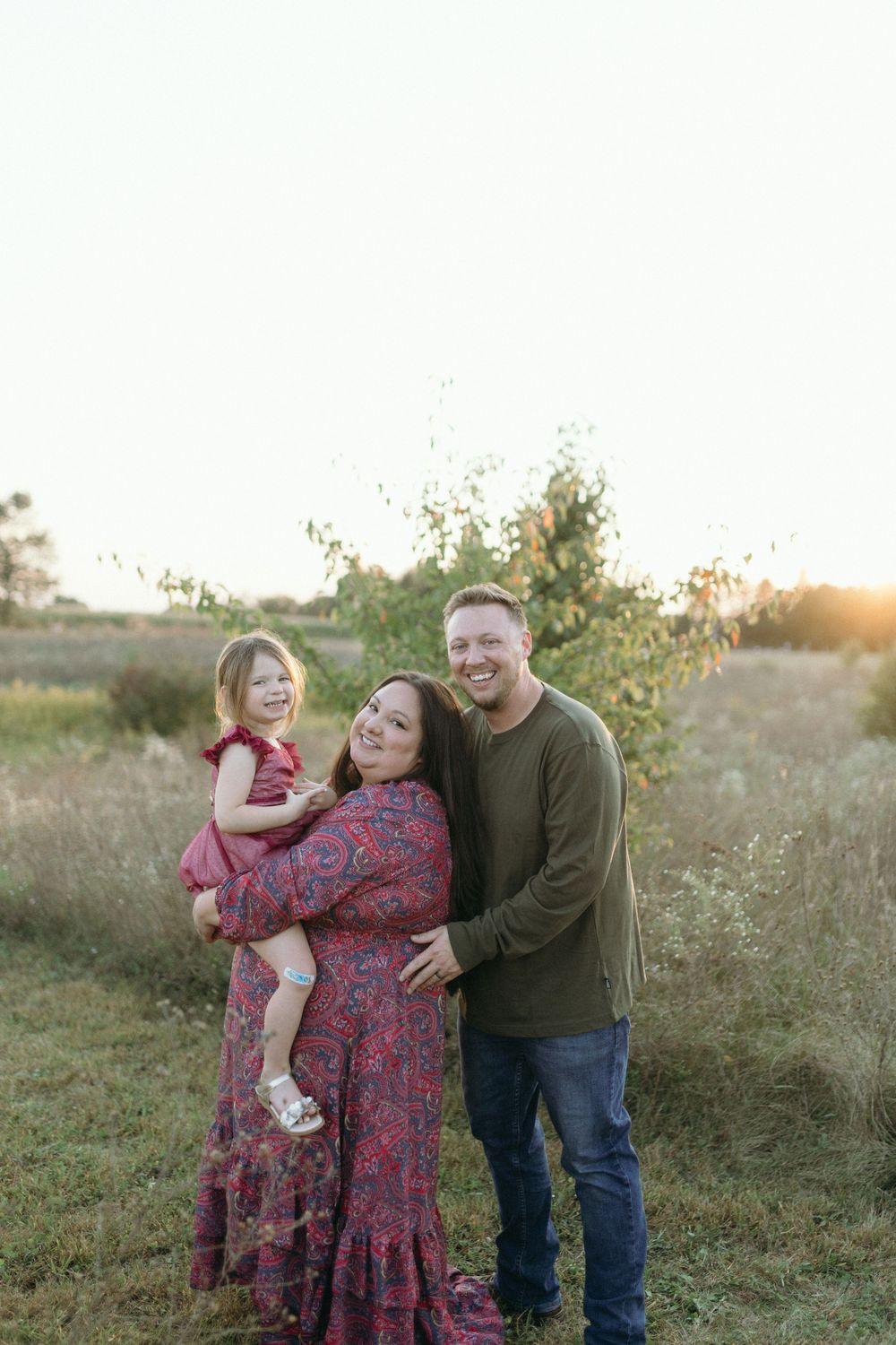 A family portrait at sunset with parents and child in coordinating outfits.