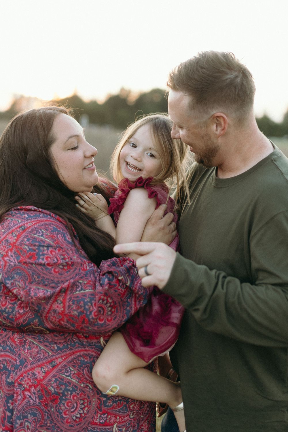 A joyful family moment outdoors with parents embracing their child at sunset.