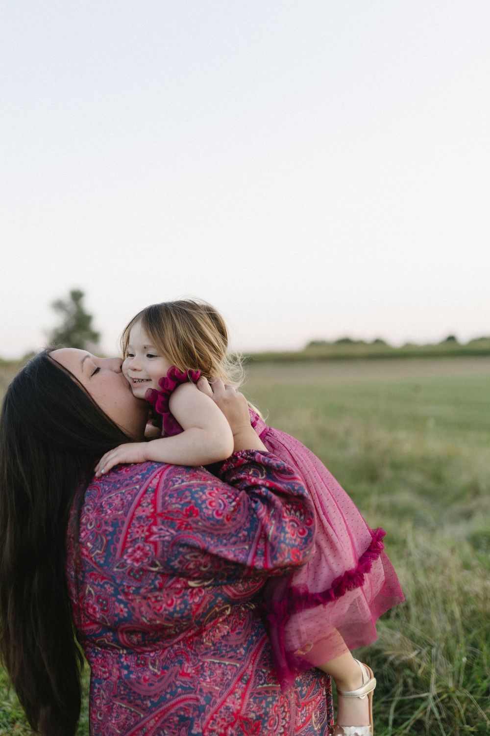 A tender moment between parent and child in a pink dress against a sunset field.