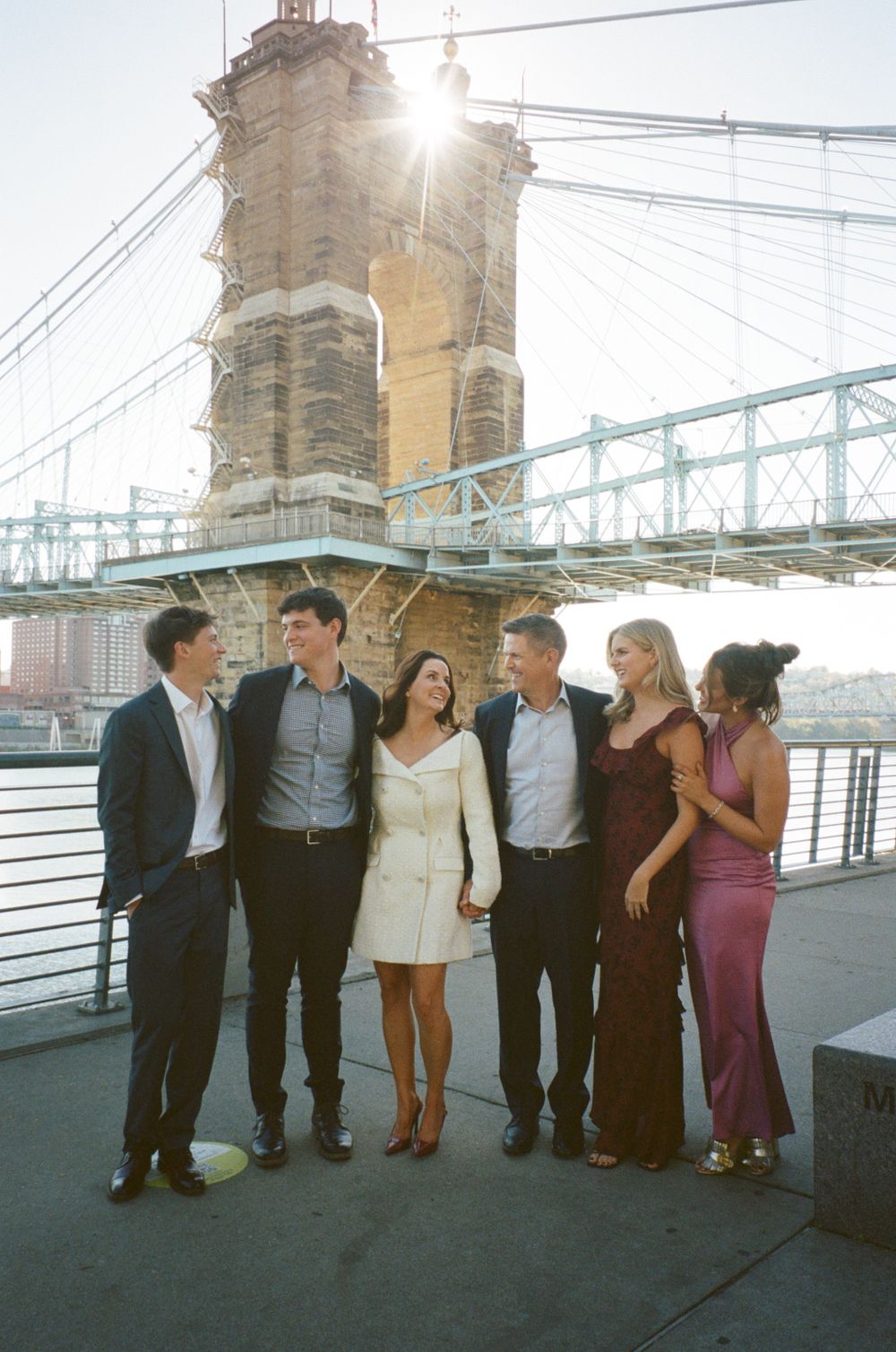 Group celebrating by a historic bridge tower during sunset wearing formal attire.