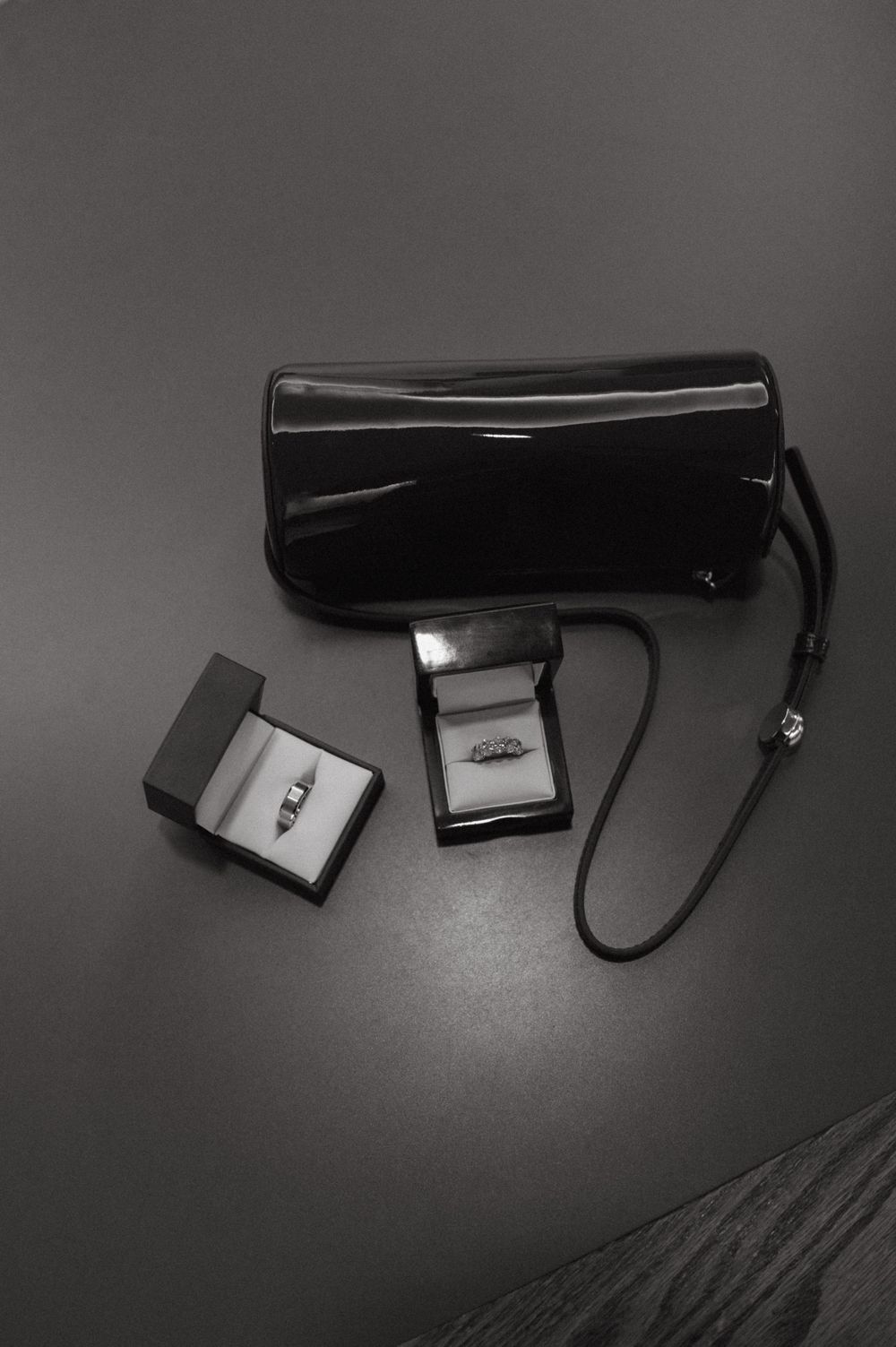 Two engagement rings in jewelry boxes displayed next to a black patent leather purse.
