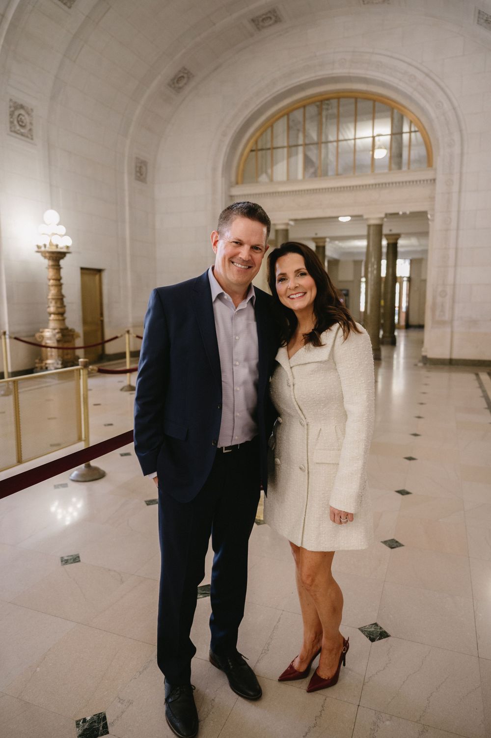 Couple in formal attire posing in an elegant white marble hallway.