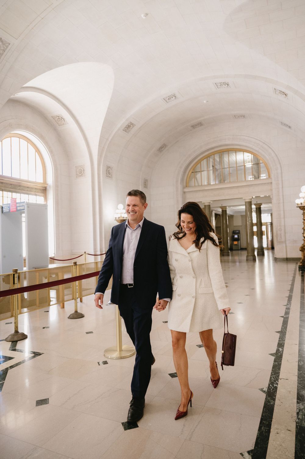 Two people strolling through an elegant white hallway with vaulted ceilings.