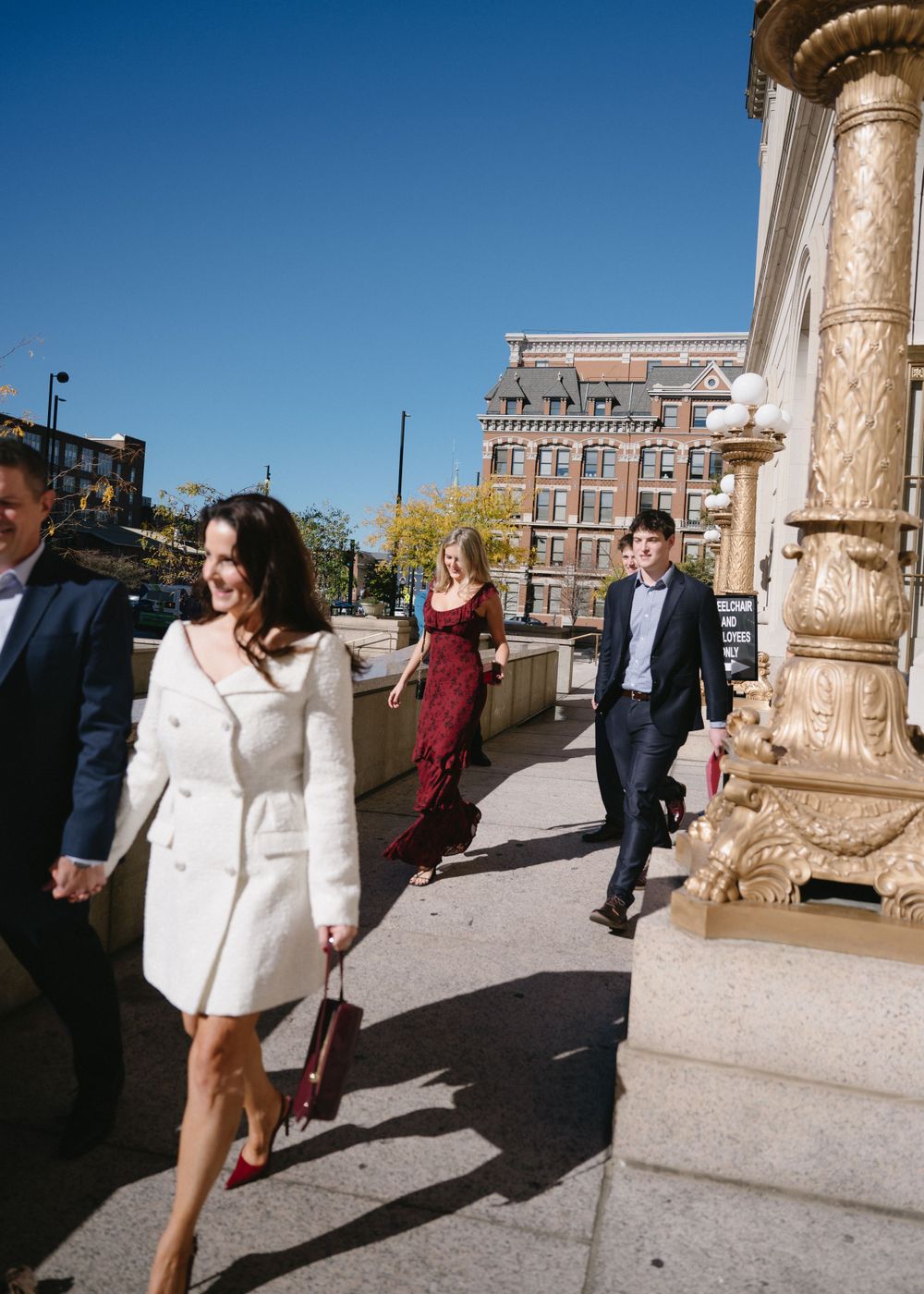 Group walking outside a historic building with ornate columns on a bright day.