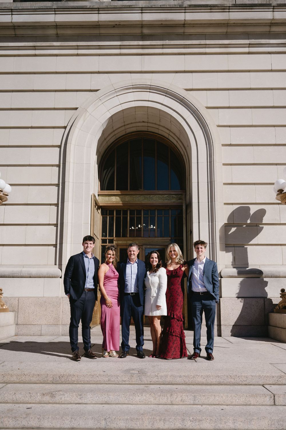 Group photo of formally dressed people standing in front of an ornate archway entrance.