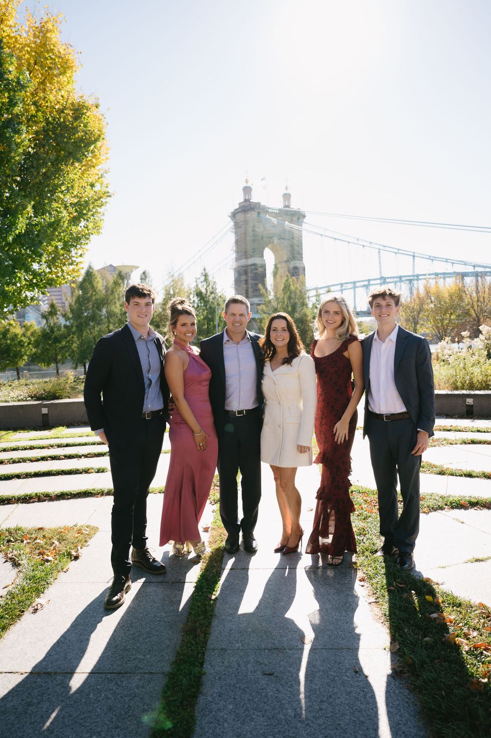 Group poses for formal photo with autumn trees and historic bridge in background.