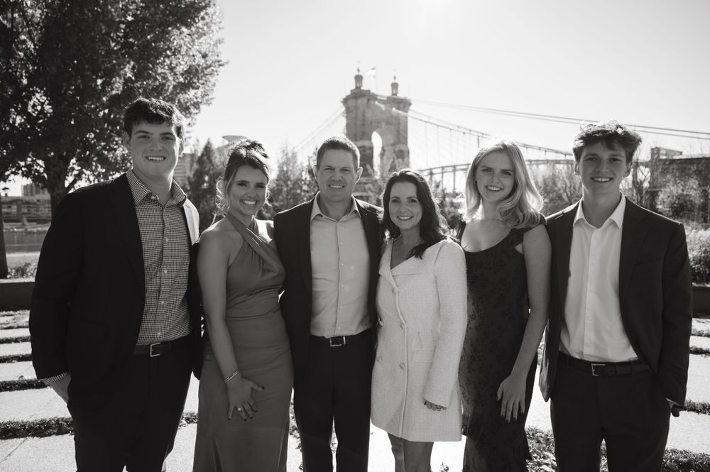 A black and white photo of a group posing in front of a bridge tower on a sunny day.