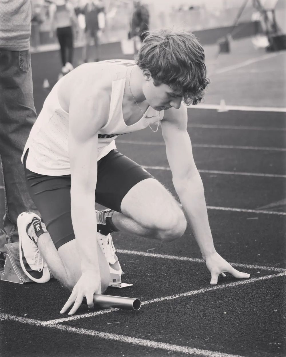 Track athlete in starting position preparing for relay race handoff on running track.