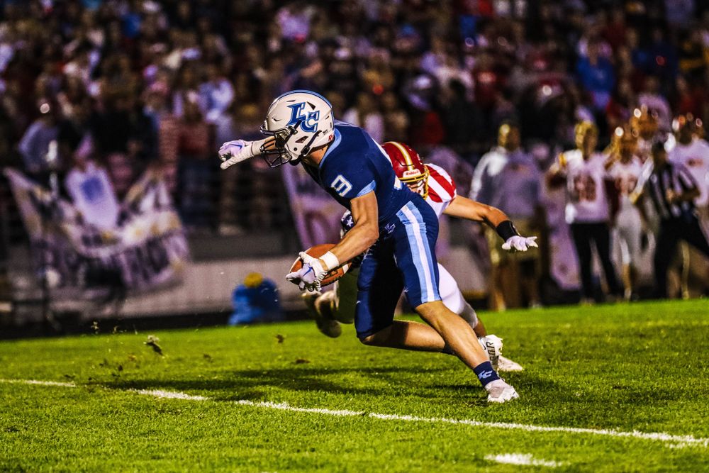 Football player in blue jersey running with ball during nighttime game.