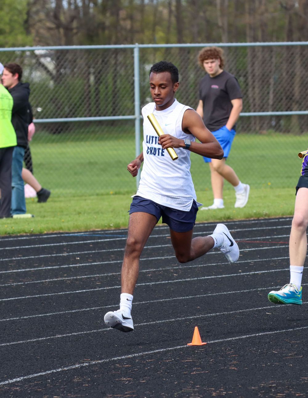Athlete in white tank top sprints on track during outdoor competition.