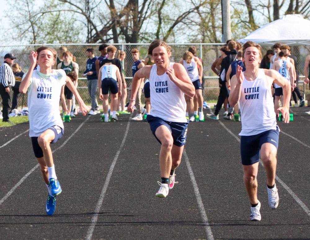 Three runners in white uniforms compete in close race on outdoor track.