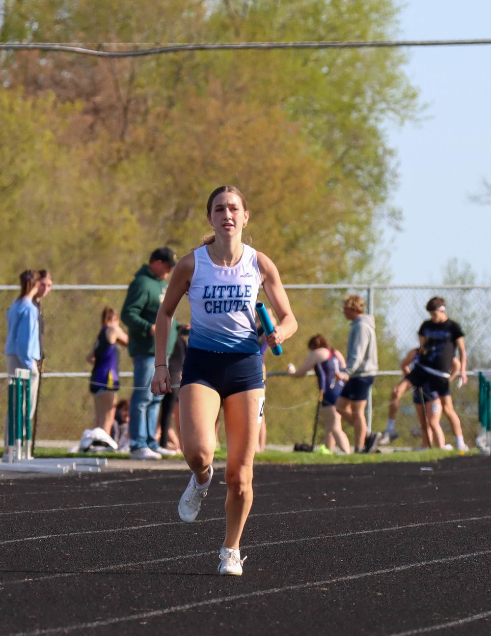 Runner in white Little Creek uniform competes on outdoor track during meet.