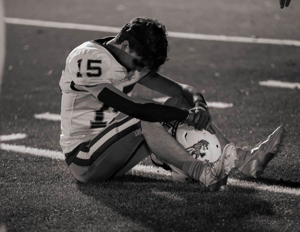 Player in jersey number 15 sits on football field in black and white photo.