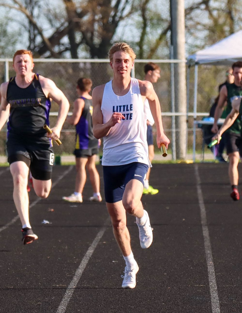 Track athlete in white uniform sprinting during outdoor competition.