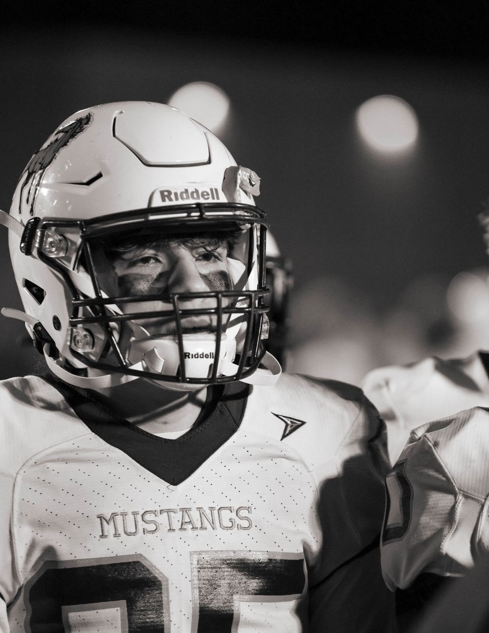 High school football player in white Mustangs uniform and Riddell helmet in black and white portrait.