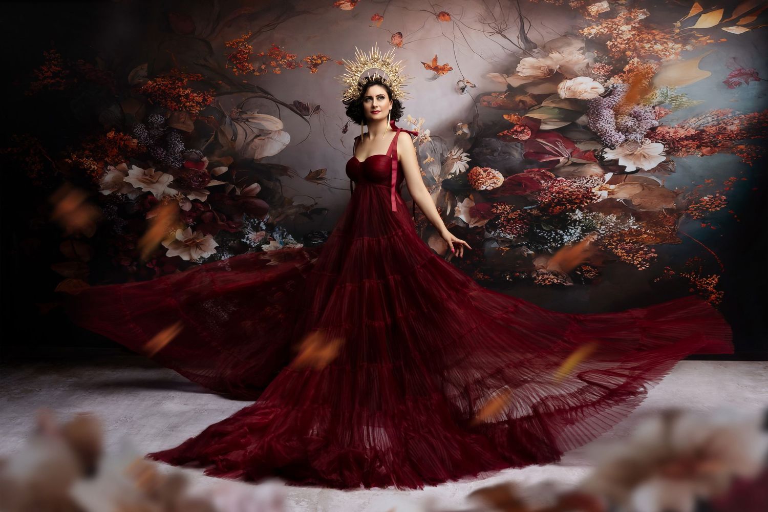 A person in a flowing burgundy gown poses gracefully amidst autumn leaves and a dark moody backdrop.