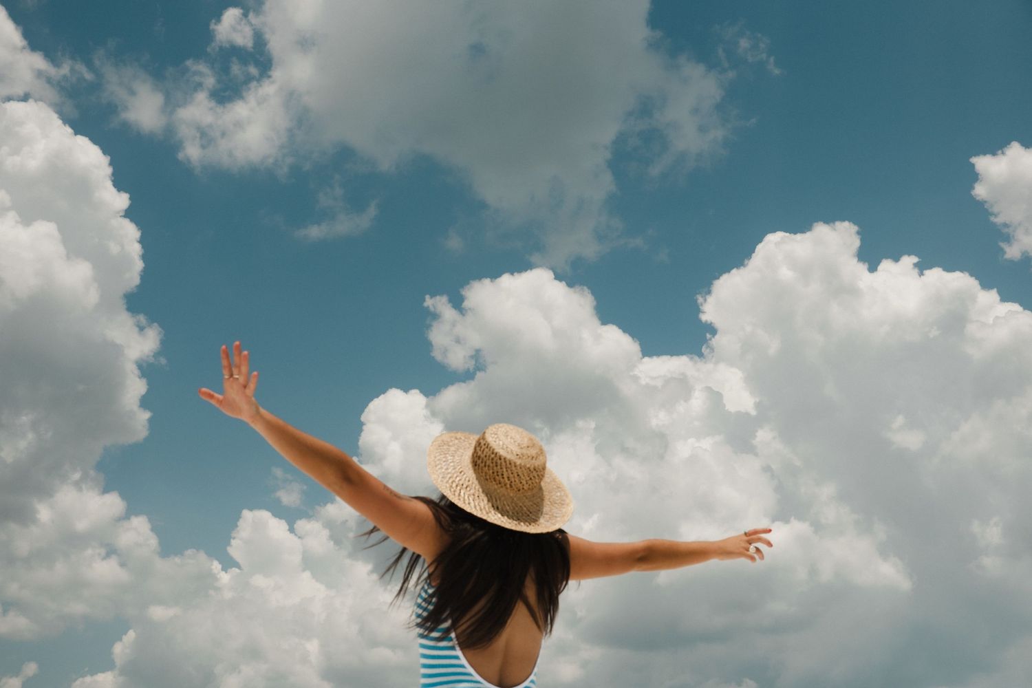 Person with arms outstretched against a dramatic blue sky with fluffy white clouds.