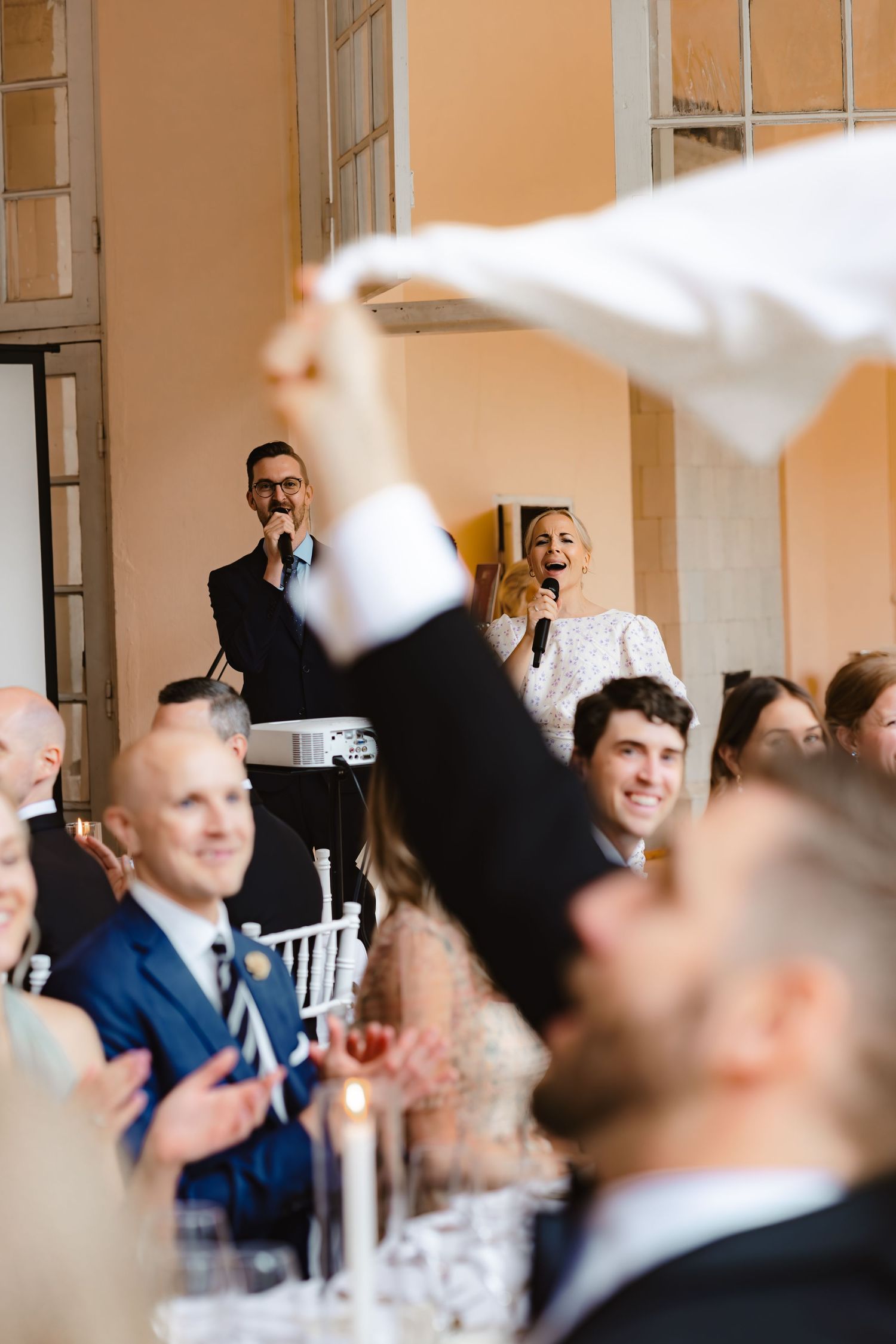 Toastmaster och toastmadam pratar i mikrofoner medan en gäst viftar med sin linneservett.