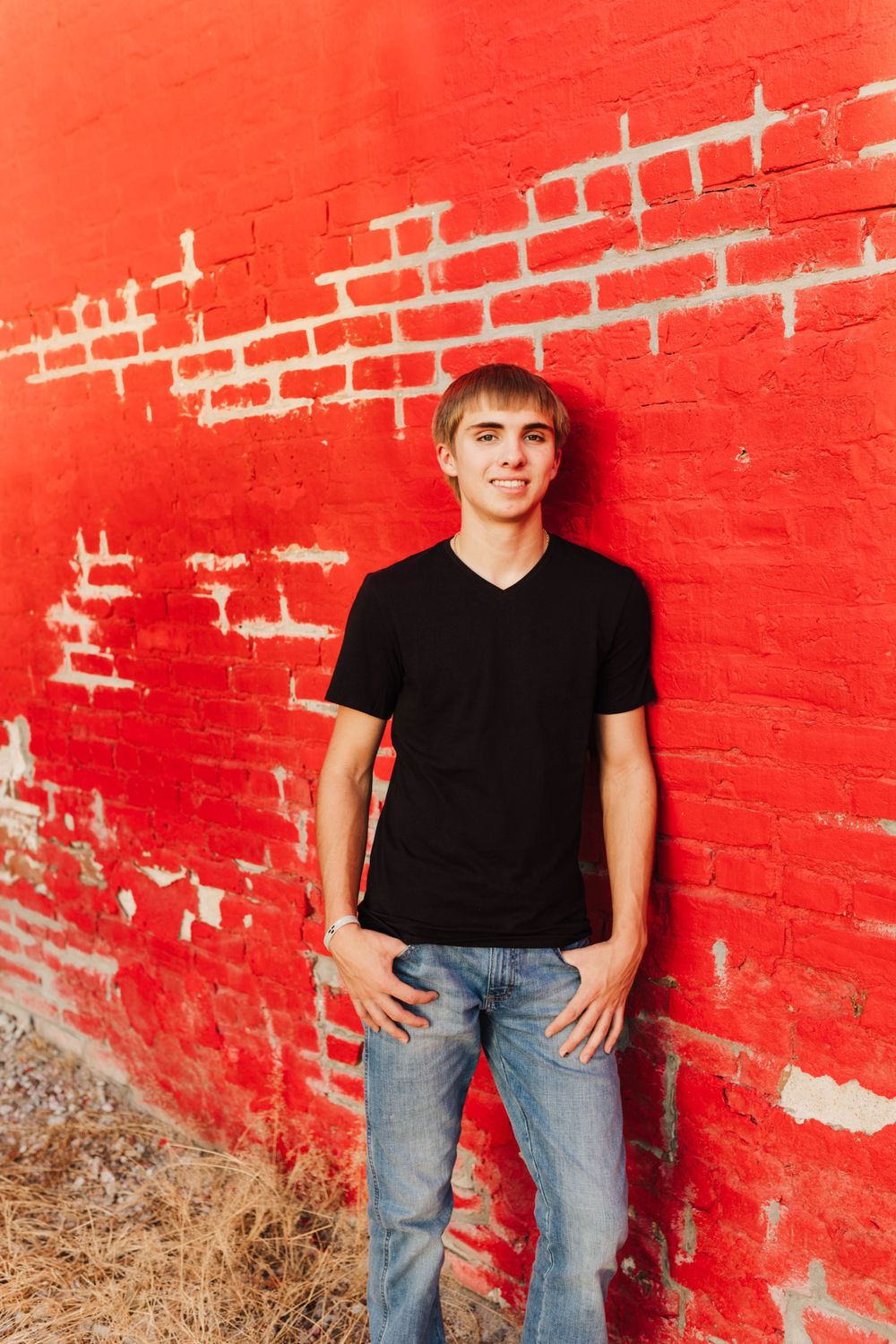A relaxed portrait against a vibrant red brick wall in casual attire.