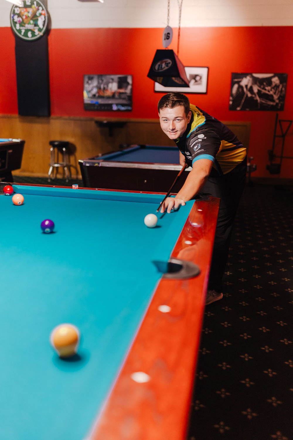 A player lines up a shot at a pool table in a game room with red walls.