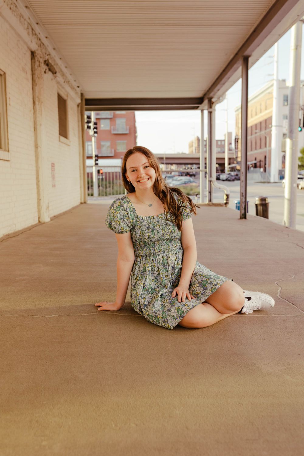 A casual portrait on a covered porch wearing a floral dress and white sneakers.