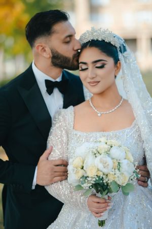 A romantic wedding portrait showcasing a sparkling white dress with a pearl necklace and white rose bouquet.