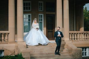 A wedding couple poses on grand stone steps of a historic building with columns.