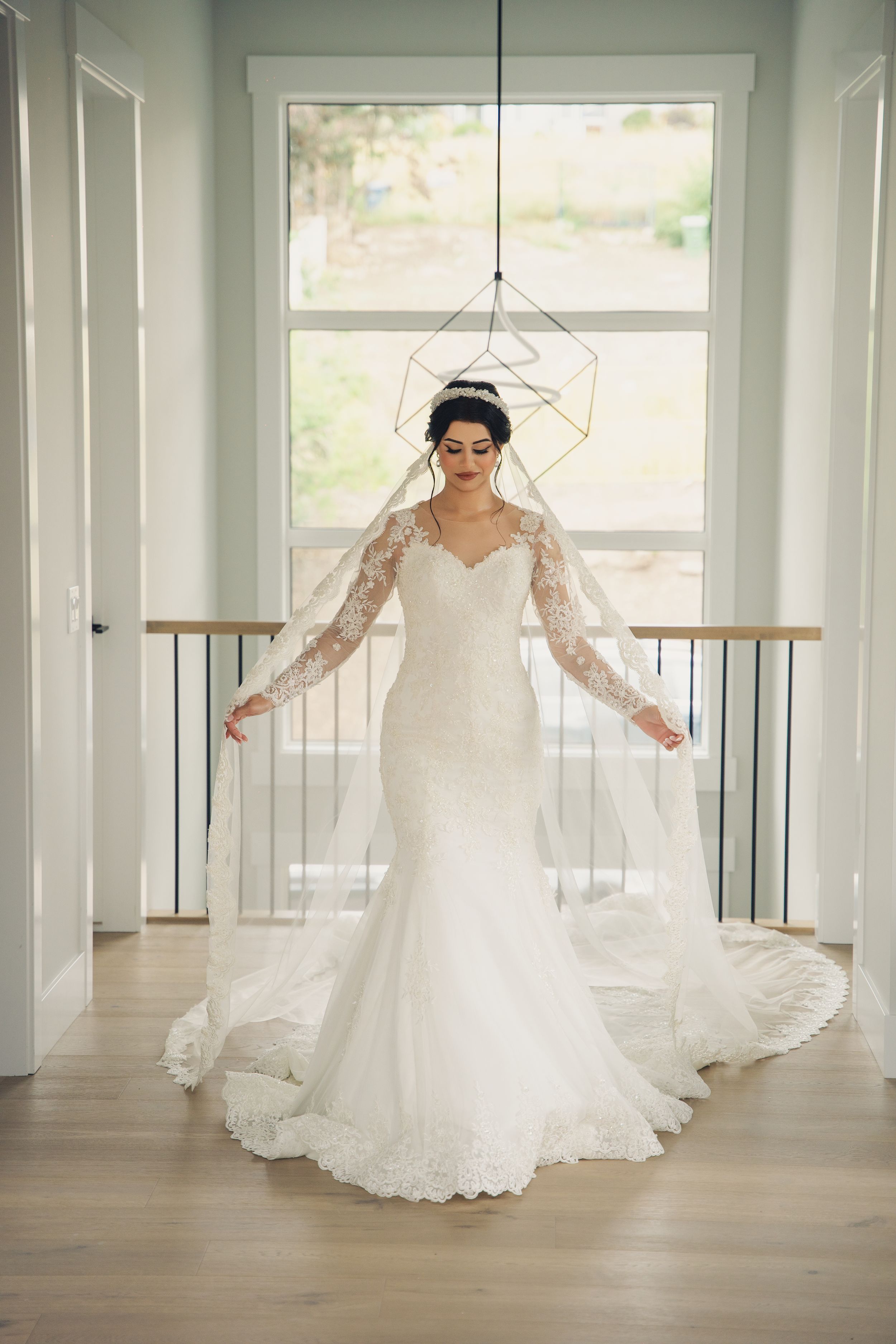 Elegant lace wedding dress with long sleeves displayed in natural window light on hardwood floors.