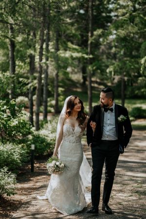 Candid wedding portrait of couple walking along a tree-lined forest path.