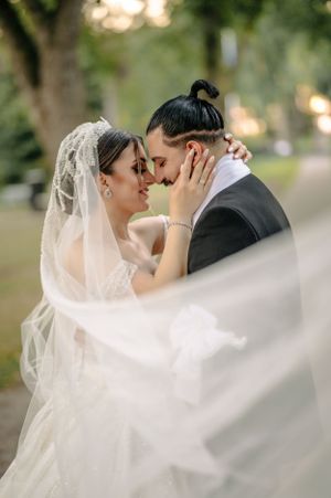 Romantic wedding moment captured through flowing veil in garden setting.