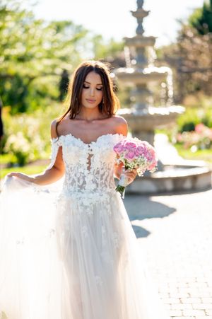 Dreamy bridal portrait near garden fountain featuring off-shoulder lace wedding gown.