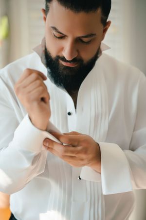Groom adjusting cuffs of crisp white tuxedo shirt during wedding preparations.