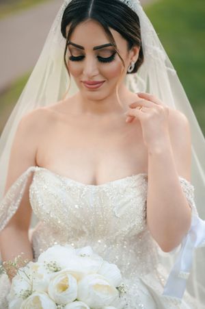 Close-up of bride wearing crystal-embellished strapless gown and veil with white bouquet.