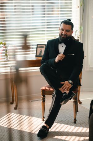 Classic pre-wedding portrait of groom relaxing in formal attire by sunlit window.