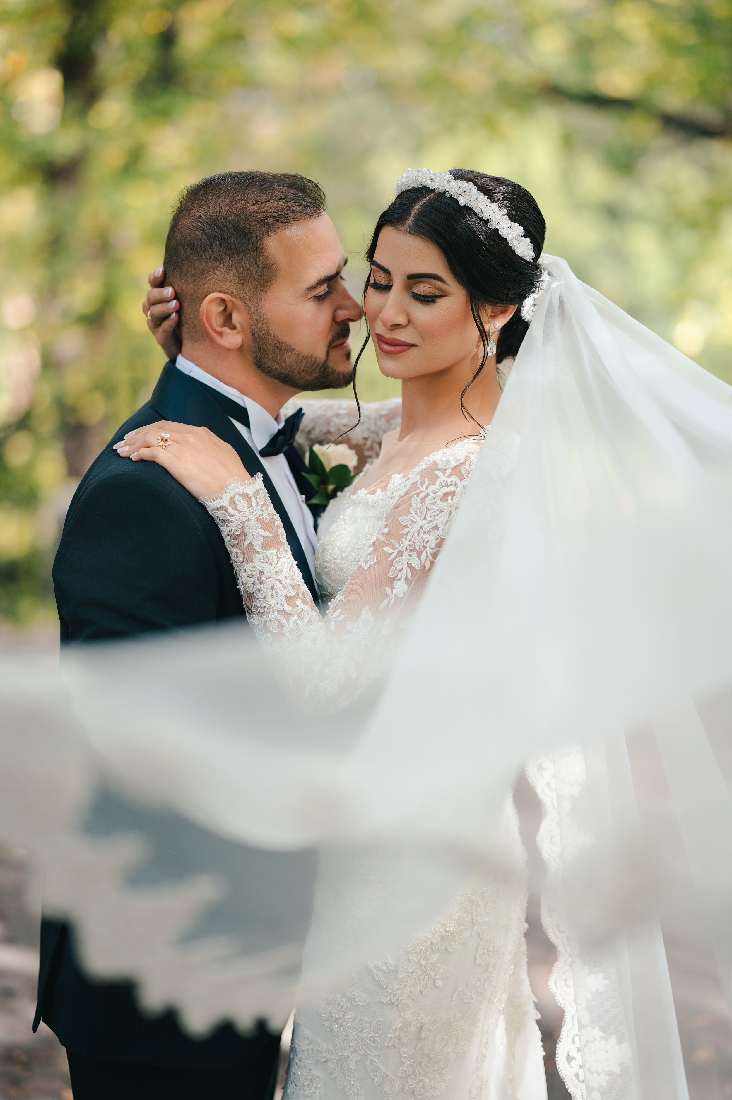 Intimate wedding portrait with flowing veil against soft outdoor bokeh background.