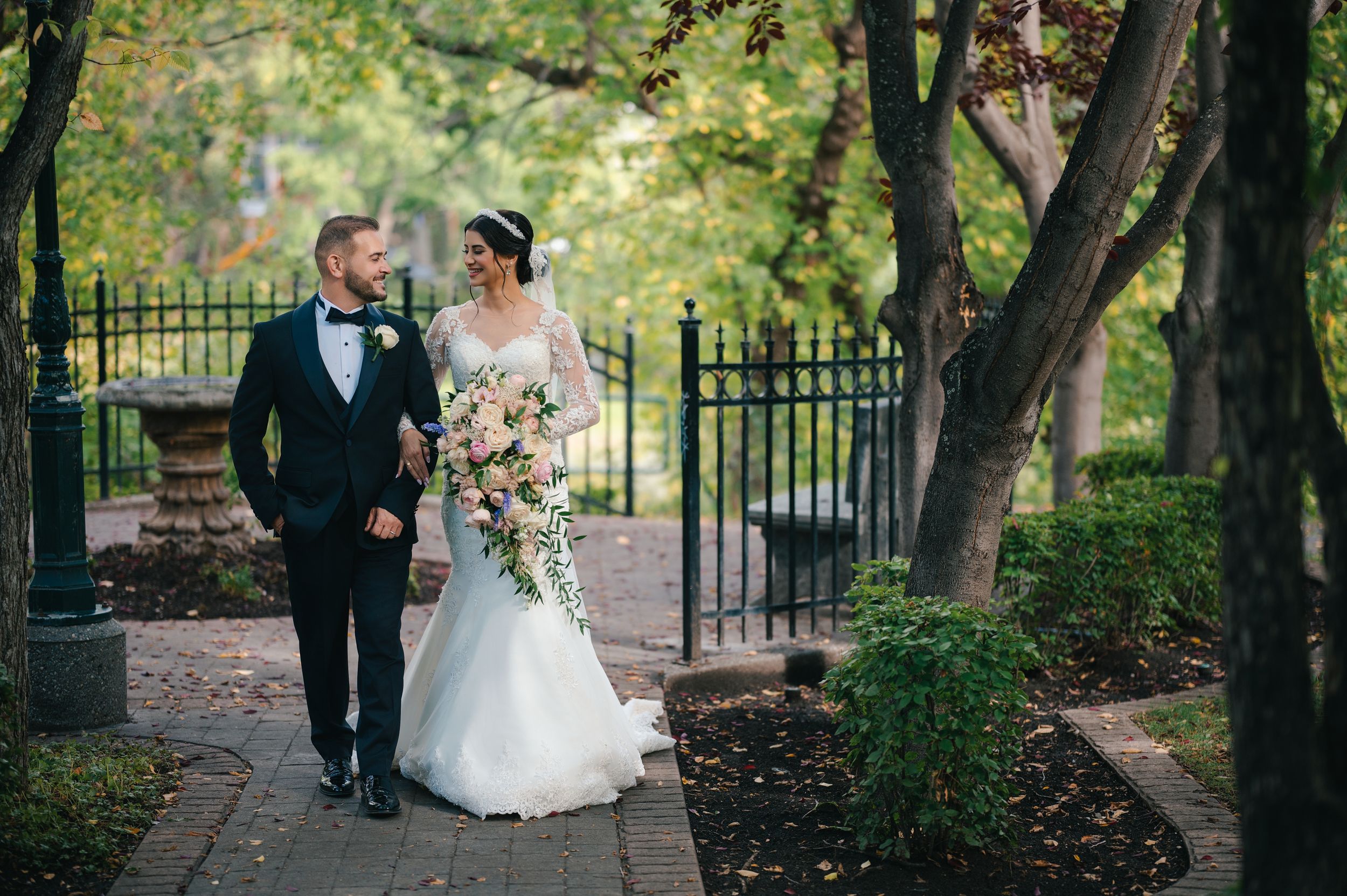 Romantic wedding couple walking along garden path with wrought iron fence.