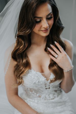Close-up bridal portrait highlighting wavy hair, jewelry and intricate lace dress details.