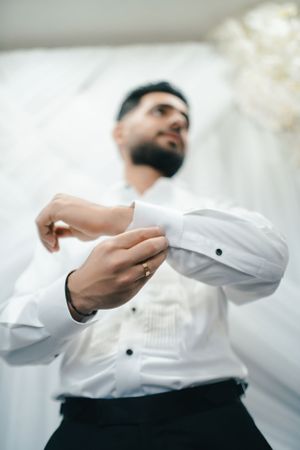 Close-up of formal white dress shirt sleeve being buttoned during wedding preparation.