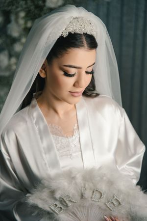 Close-up portrait of a bride in white satin robe with delicate veil and elegant makeup.